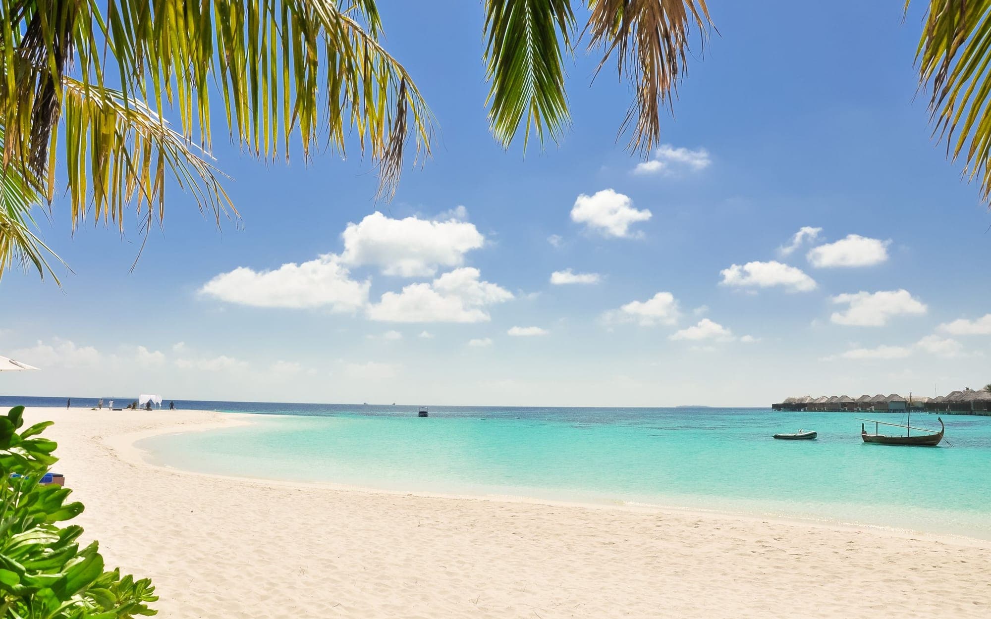 Seven Mile Beach shallows at midday — clear turquoise water, a small boat heading for Booby Cay