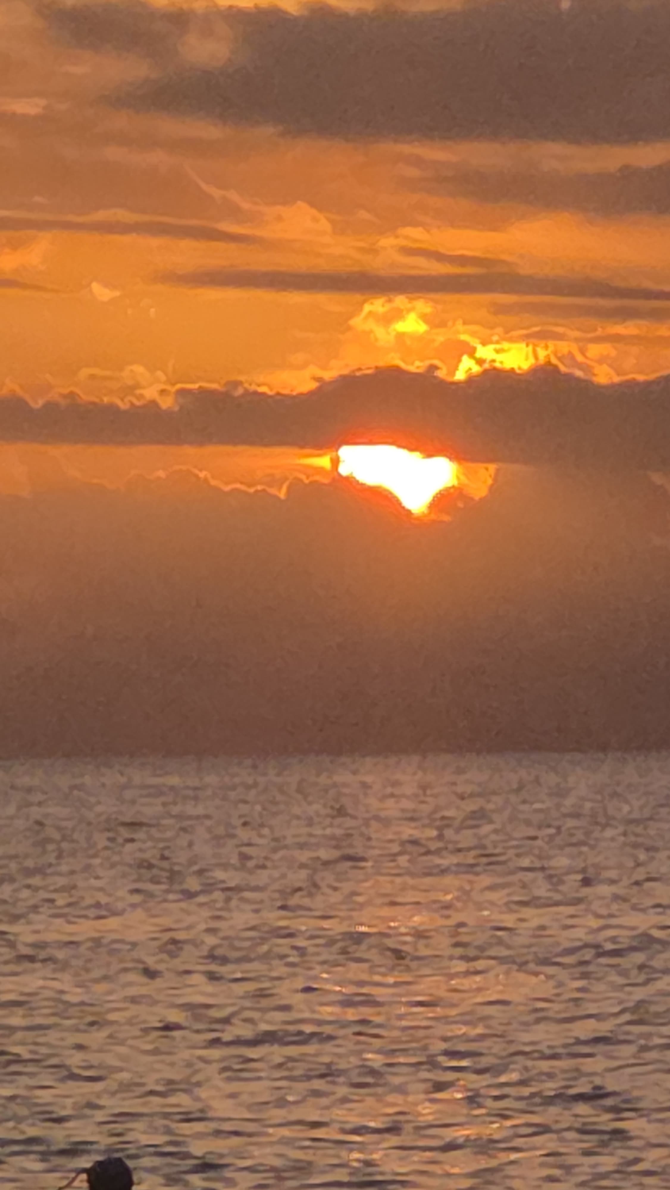 The sun dropping into open sea through banded cloud, seen from the cliff